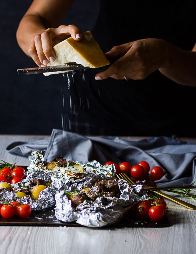 A hand grating Parmesan cheese over the ready foil packets
