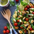 A half plate of salad showing the wooden spoons and tomatoes on the side