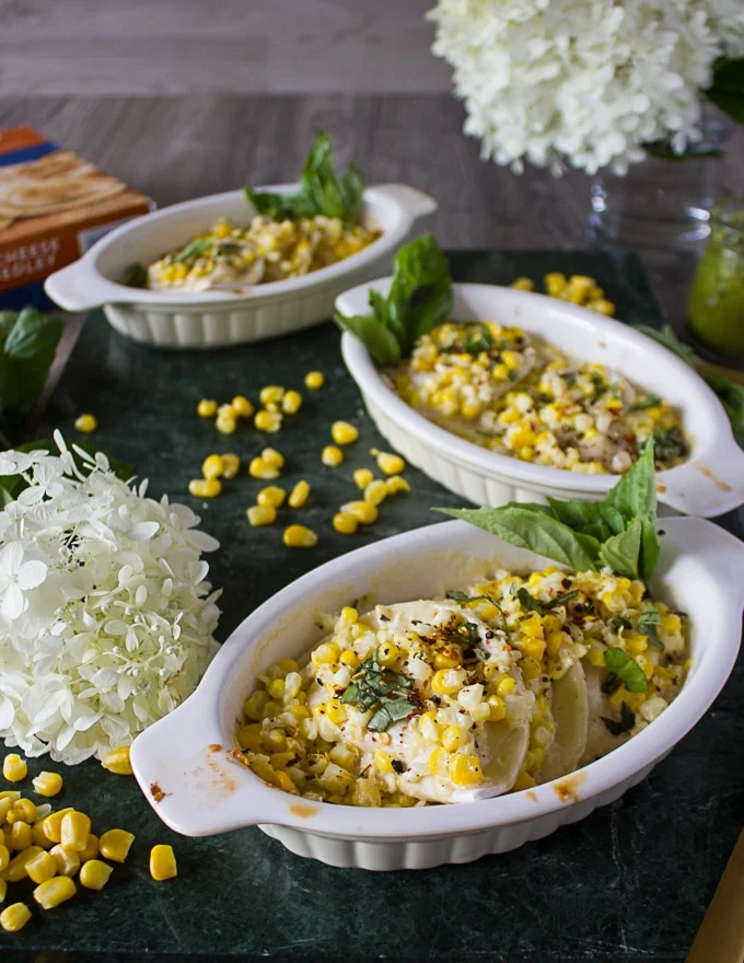 three ramekins of corn casserole surrounded by corn kernels, white flowers on a marble