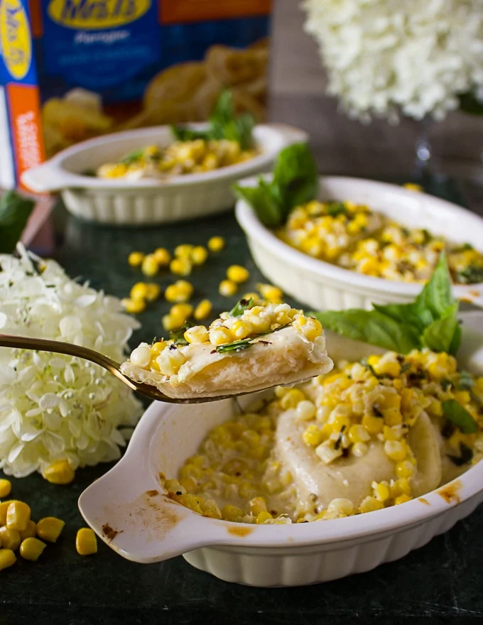A hand holding a spoon with a bitten pierogy from the corn casserole