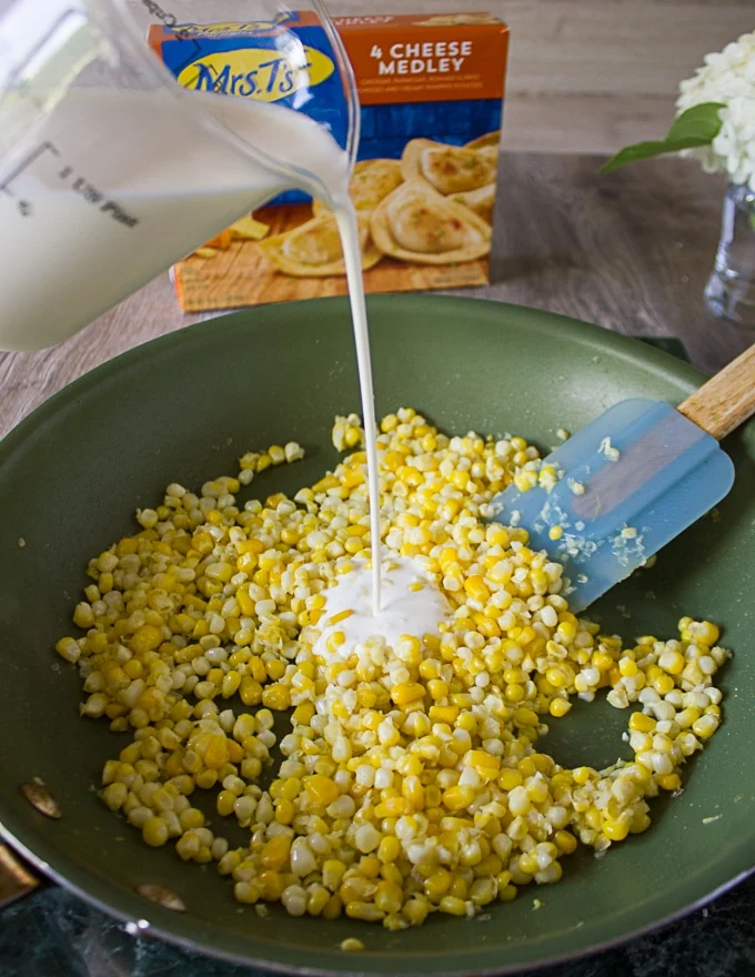 Corn kernels cooking in the garlic butter skillet and cream being added over it