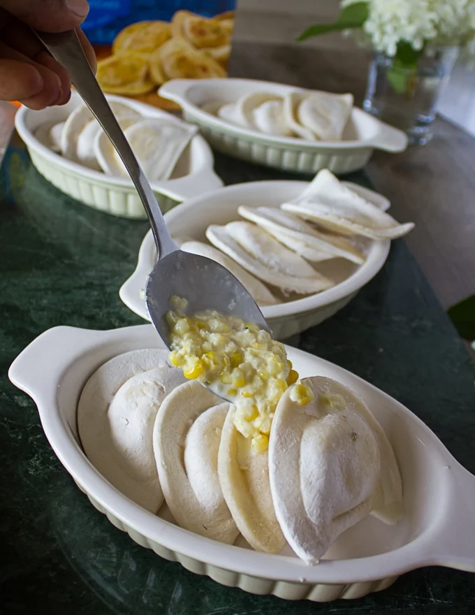A spoon pouring the corn mixture over pierogies in a ramekin