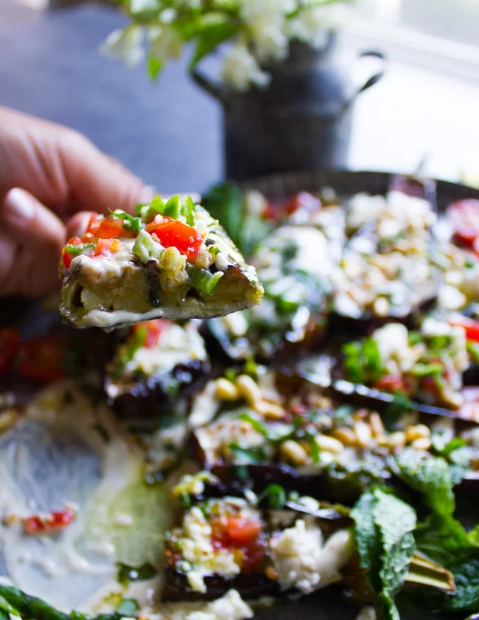 A hand holding a cut off eggplant half to show the inside texture with all the toppings