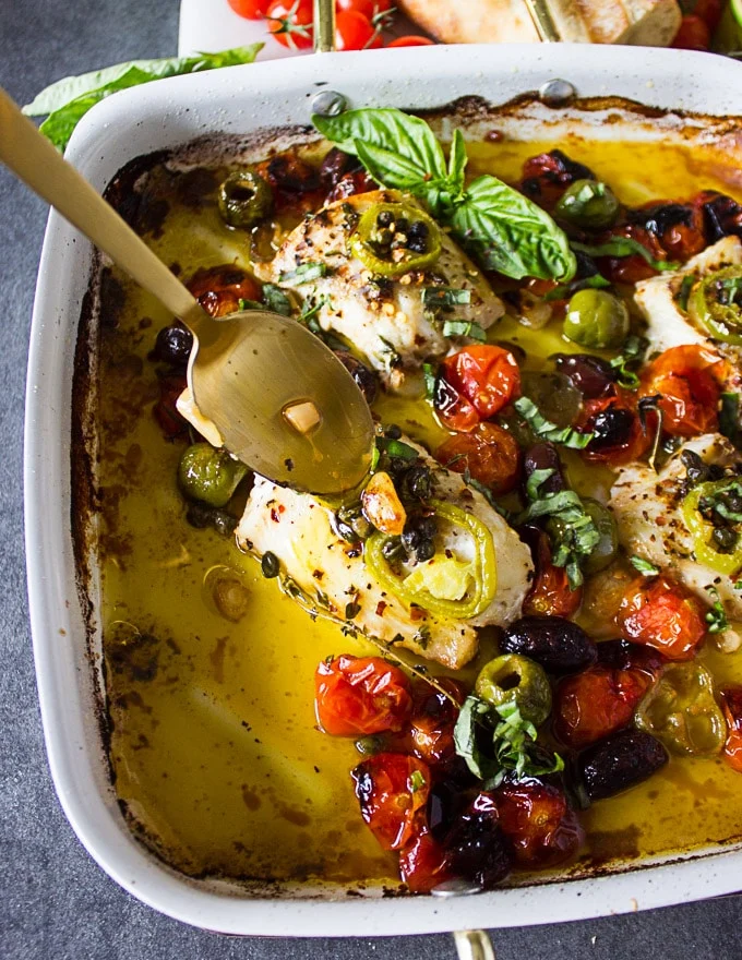 A spoon drizzling the juices and olive oil over the baked fish