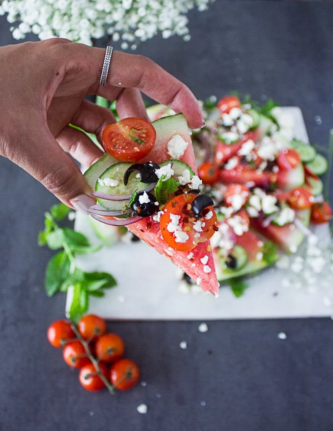 A hand holding a wedge of watermelon feta salad