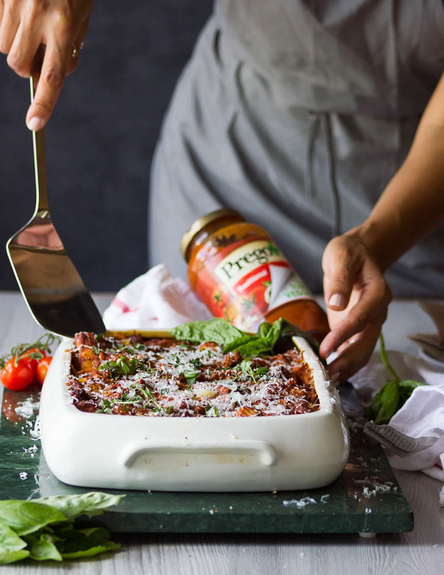 A hand holing a serving spoon and about to serve the baked ziti right our of the oven