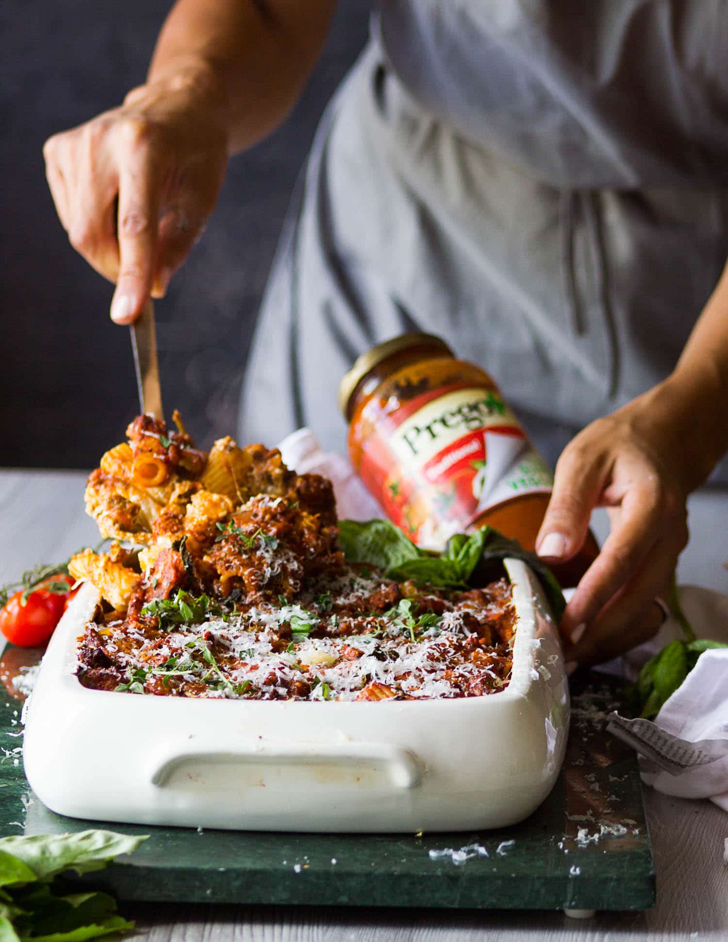 A hand serving the baked ziti right our of the pan using a spoon showing the cheesy baked ziti pasta and sauce