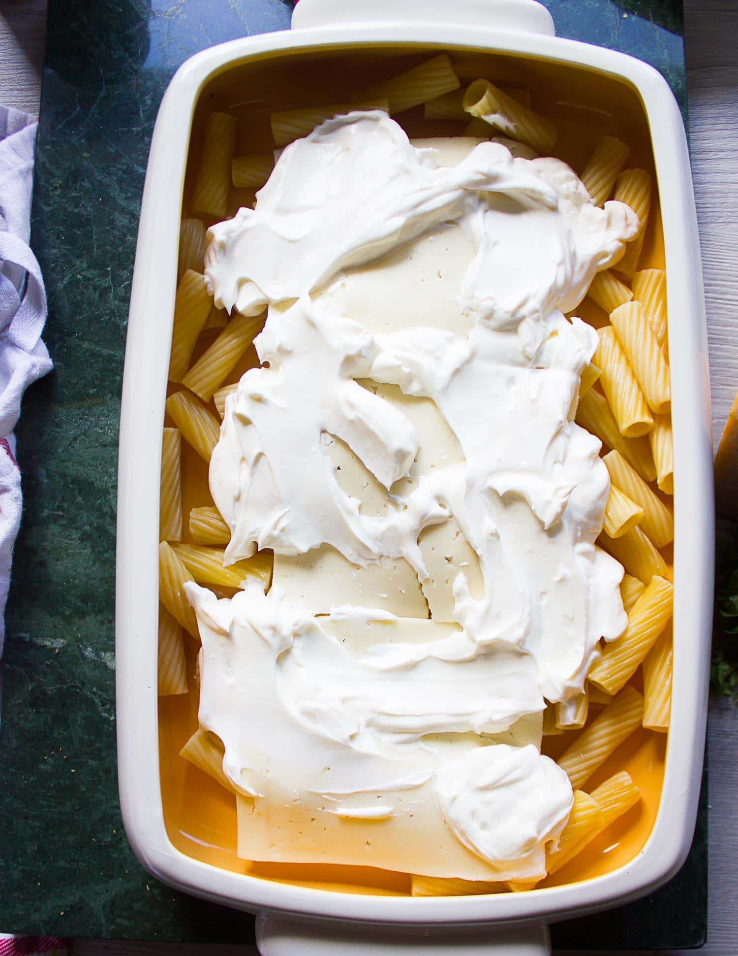 The layering of baked ziti in a baking dish. Here it shows pasta at the bottom followed by cheese and sour cream