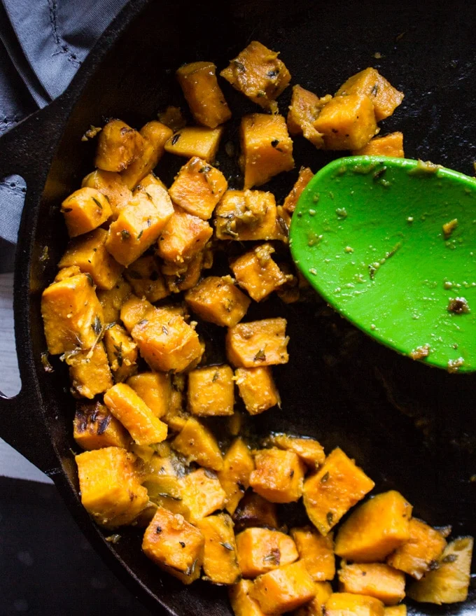 A pan and spatula cooking the sweet potatoes in a skillet