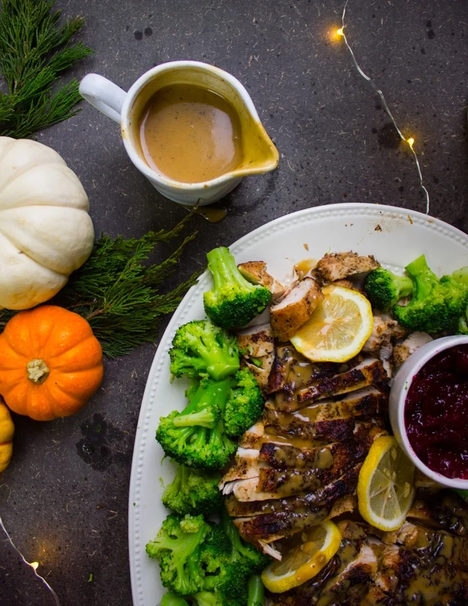 A gravy boat with the luscious gravy made from scratch showing and some turkey breasts on the plate drizzled with gravy too.