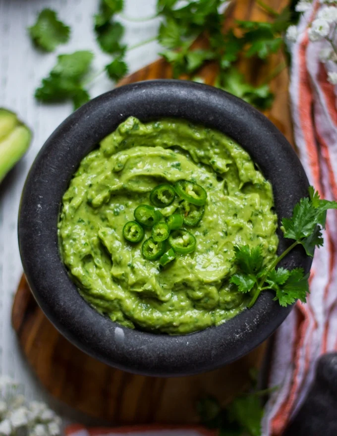 Close up of a bowl for authentic guacamole recipe topped with jalapenos