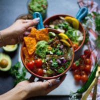 A hand holding a fajita bowl loaded with tomatoes, chips, salsa, guacamole and chicken