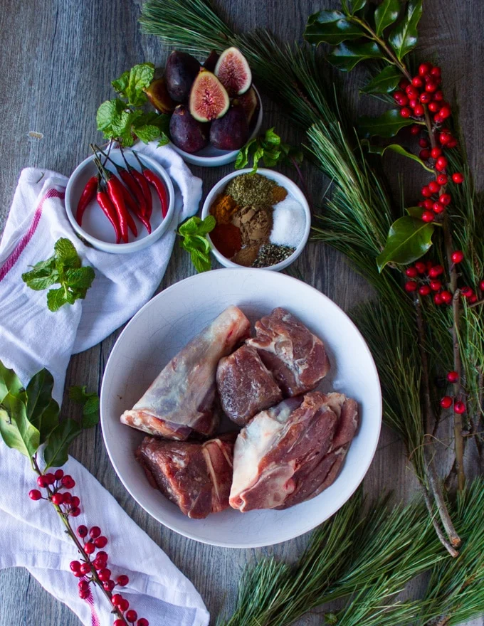 Ingredients for cooking lamb: lamb shoulder pieces cut up surrounded by a bowl of Moroccan spice, surrounded by red chillies, fresh figs and a tea towel