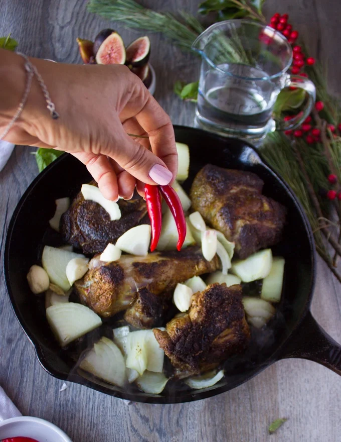 A hand adding in some spicy red chillies to the lamb skillet