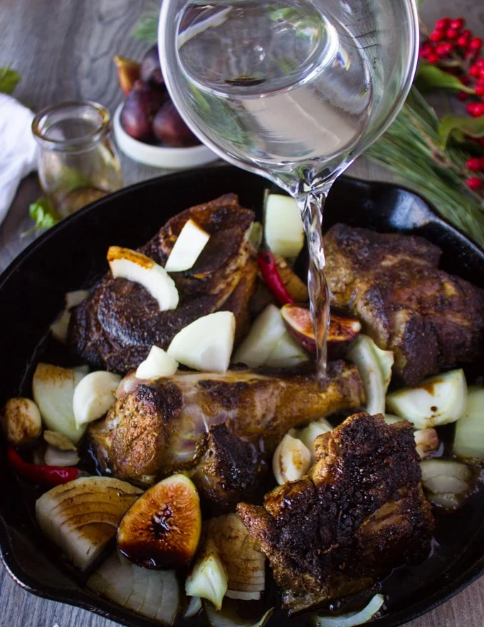 Water being poured over the lamb meat in a skillet with all the sweet and spice sauce ingredients ready to roast