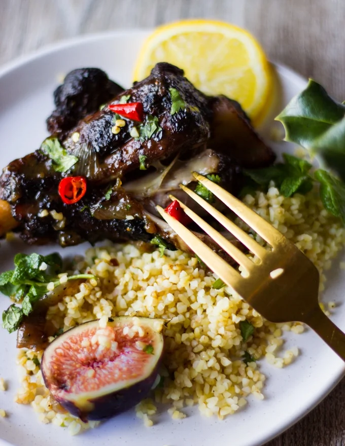 A fork eating a piece of cooked lamb with couscous and some sweet figs and spicy chillies on a plate