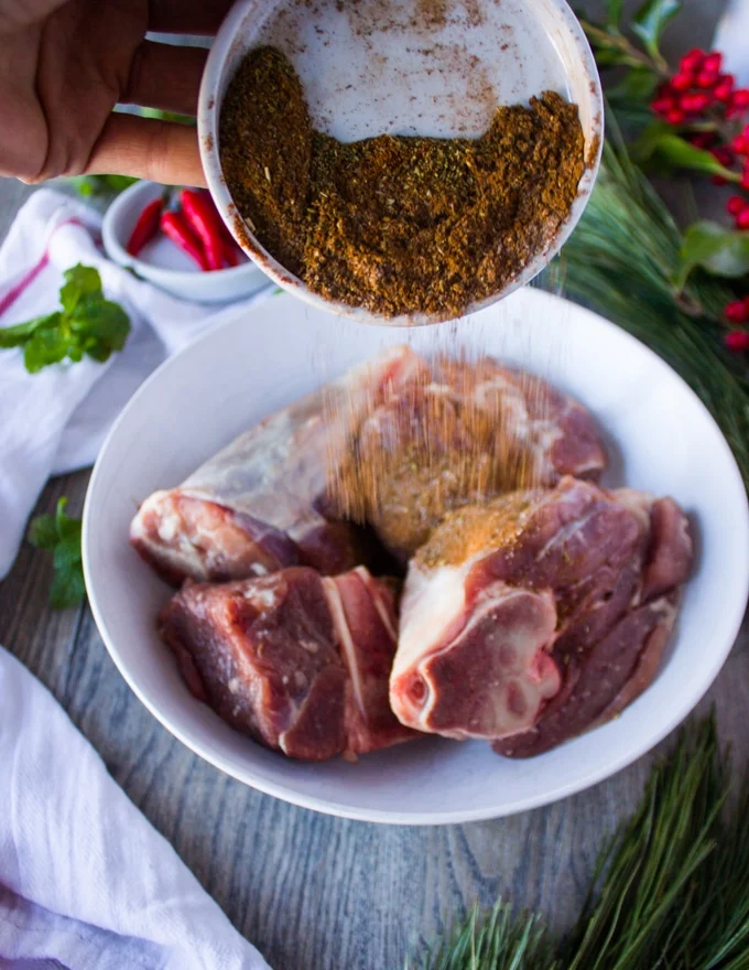 A hand pouring Moroccan spice blend over the lamb meat to season