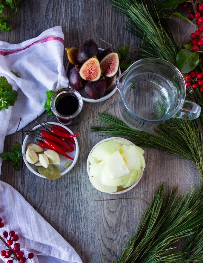 Sweet and spicy sauce ingrdients inclusing a bowl of fresh figs, sweet balsamic vinegar, onion, garlic, bay leaf, red chillies, water