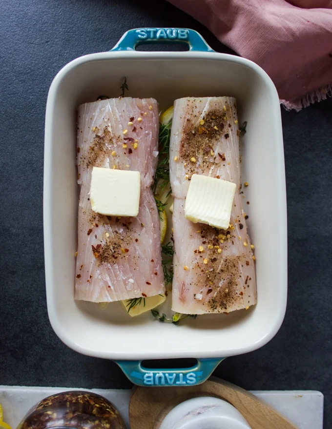 seasoned mahi mahi fish over the baking dish with a dab of butter ontop ready to go to bake in the oven