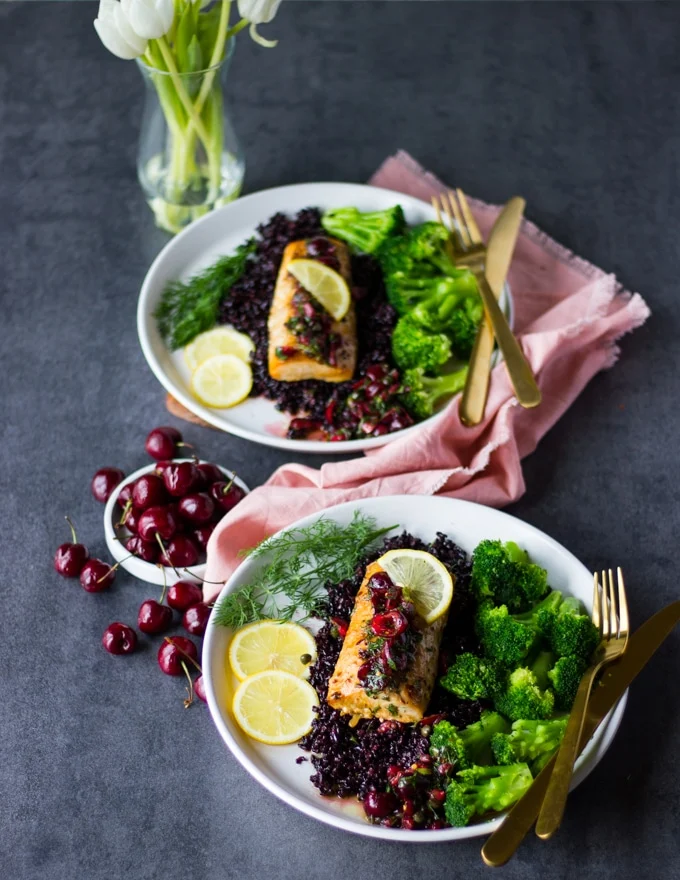 two plates of baked mahi mahi fillets over wild reice and a side of steamed broccoli served with some fresh cherries in a separate plate