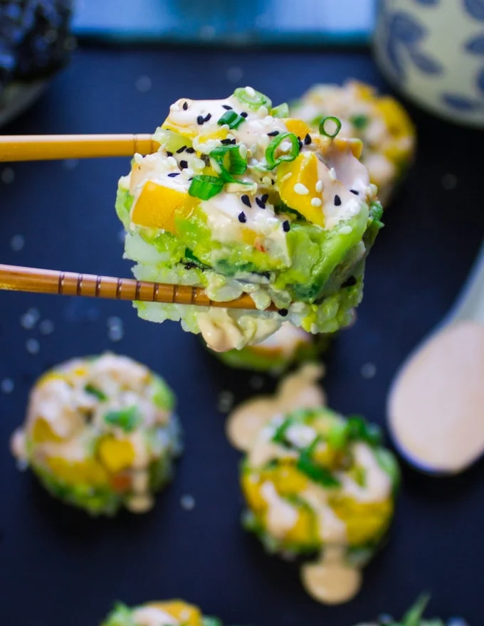 A chopstick holding a crab sushi over a plate of sushi stacks showing how to eat it and showing the layers