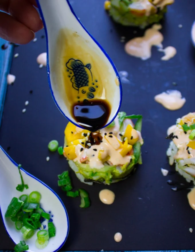 A spoon drizzling some soy sauce over the califronia rolls