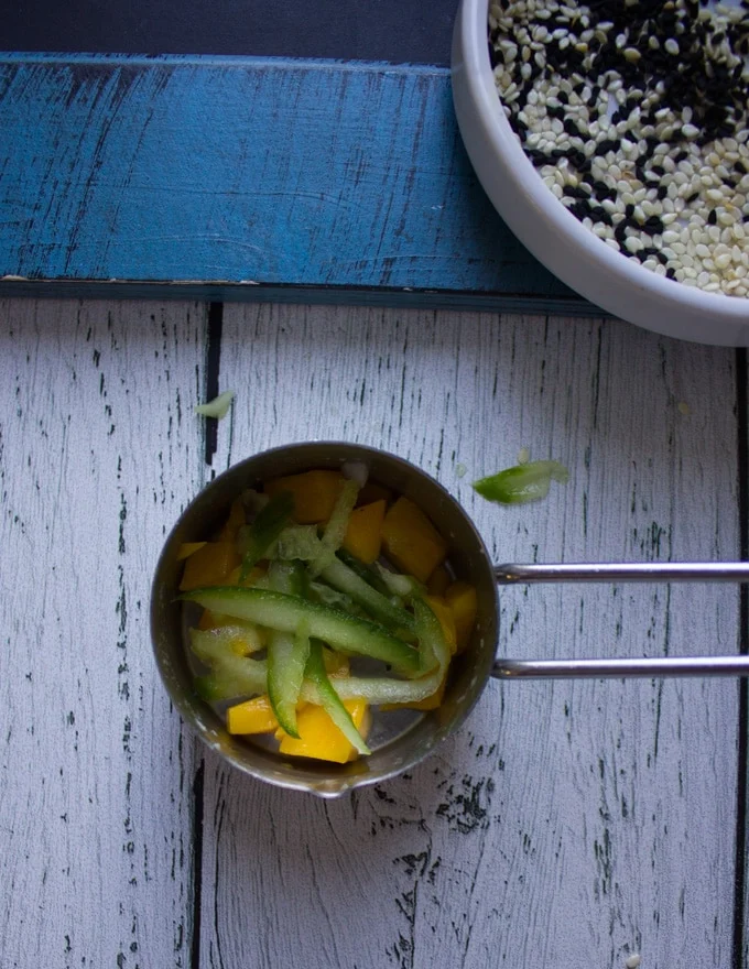shredded cucumbers added over the mango chunks in the same measuring cups layering the sushi stacks