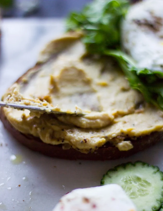 A knife spreading a generous layer of hummus over the toast bread showing the creamy texture