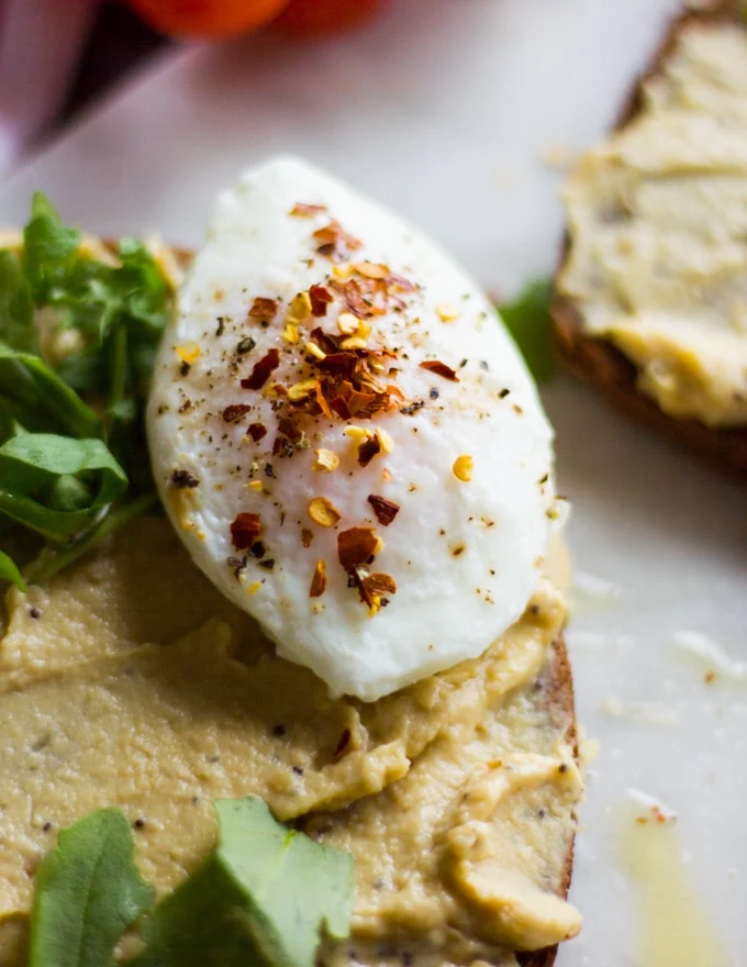 A poached egg added over the hummus layered toast with a sprinkle of salt, pepper and chilli flakes