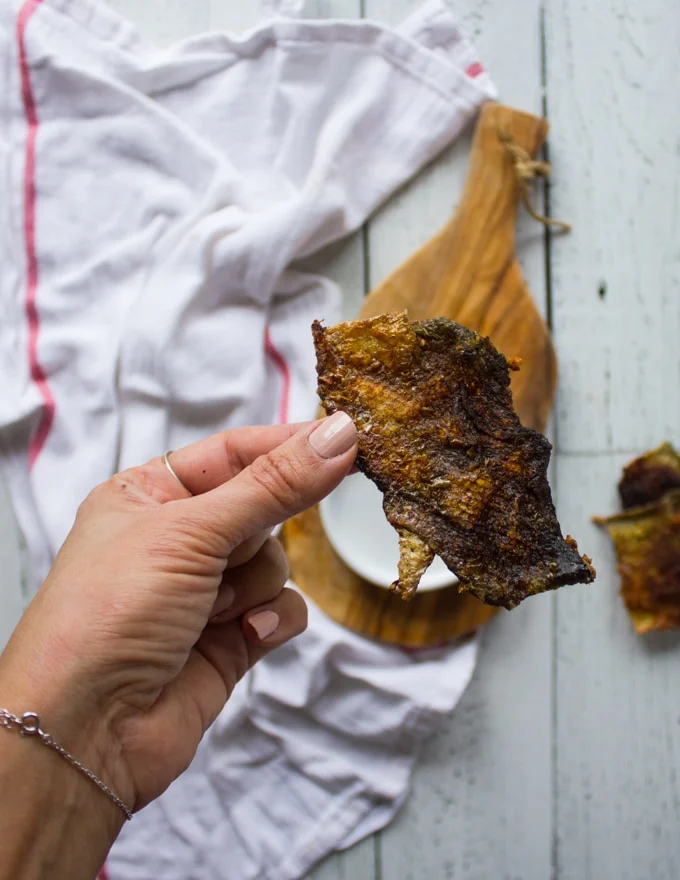 A hand holding a piece of crispy salmon skin for sprinkling over the sushi burrito