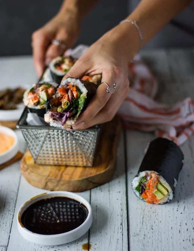 A hand holding the sushi burrito bitten up to show the bite and dipped in a bowl of soy sauce