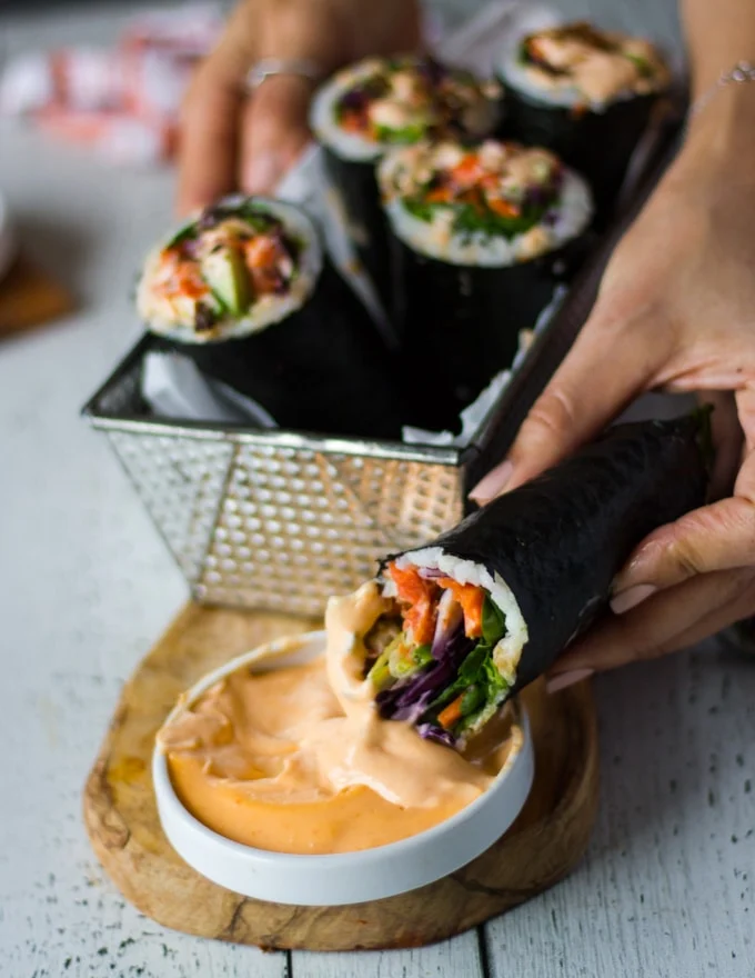 A hand dipping more sushi burrito into the spicy mayo and biting