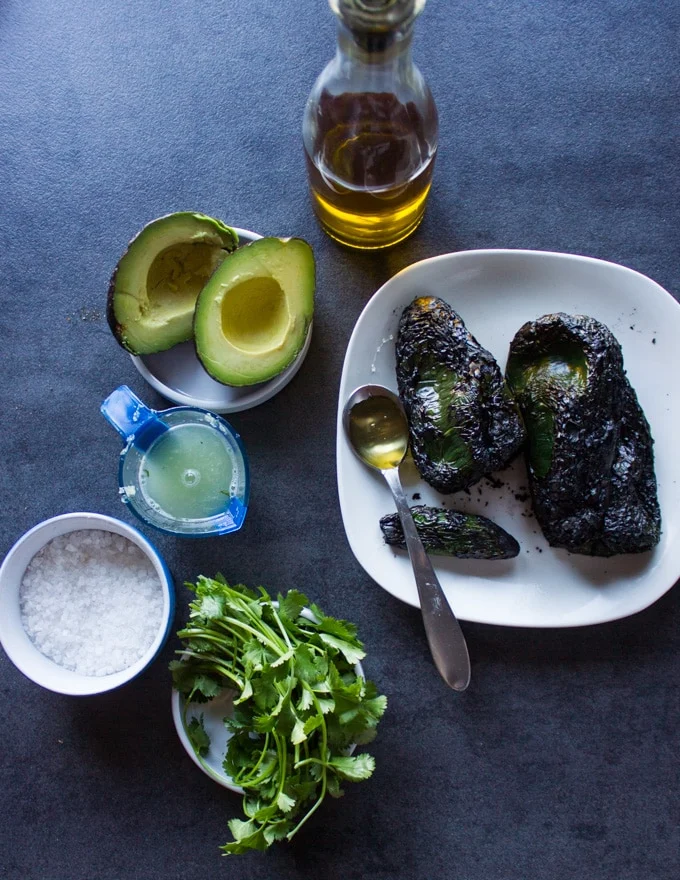 Ingredients for the poblano sauce on a board including poblano peppers, avcoado, jalapeno, lime juice, olive oil, cilantro, honey and salt