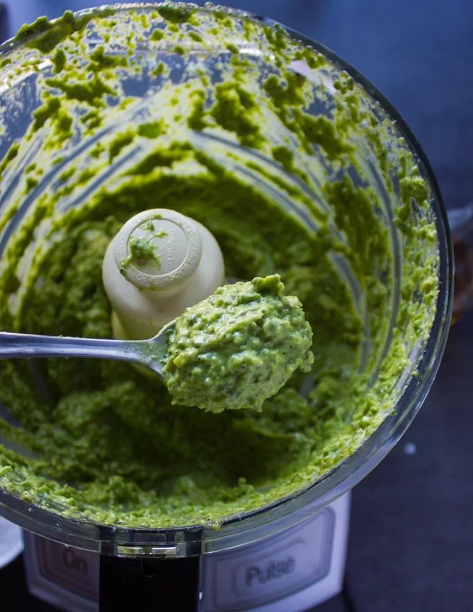 A spoon holding off a the poblano sauce in the food processor showing how smooth and creamy and ready the sauce is