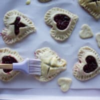A pastry brush brushing the egg wash over the tops of the cherry pies