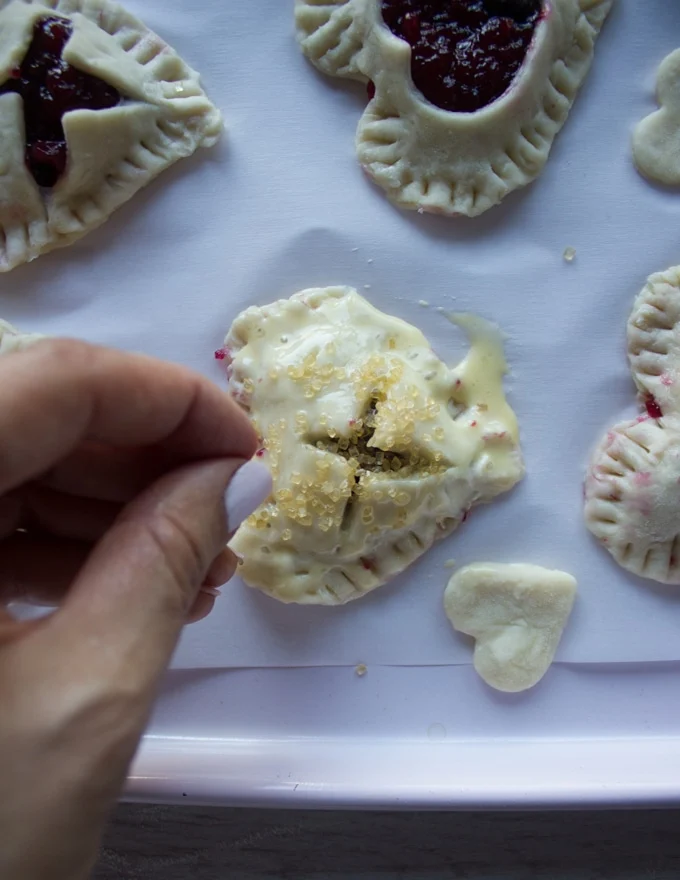 A hand sprinkling coarse sugar over the tops of the pie crust before baking