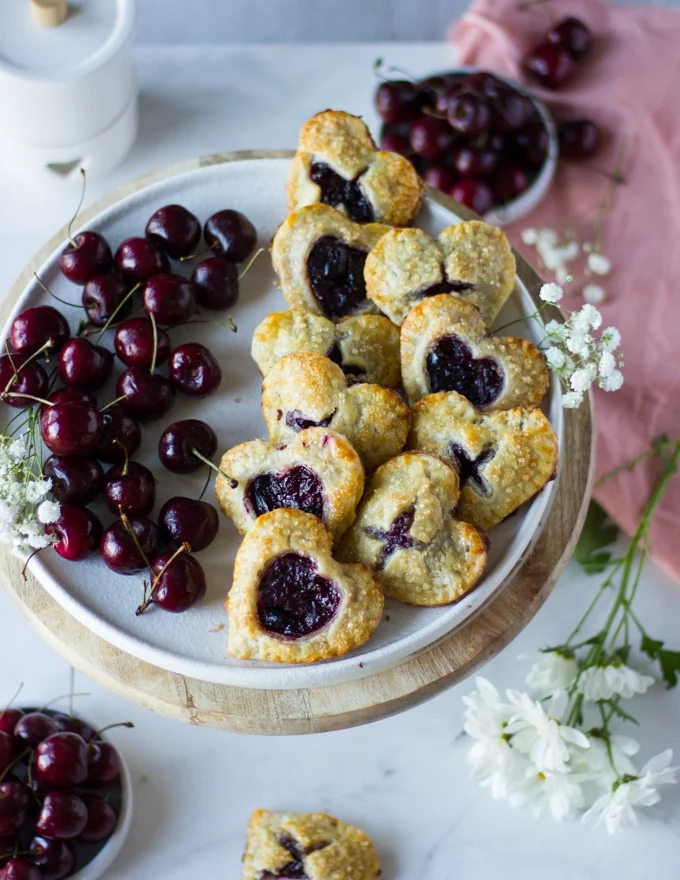 Top view of the plate of sweet cherry pies on a side and fresh cherries on the other side.