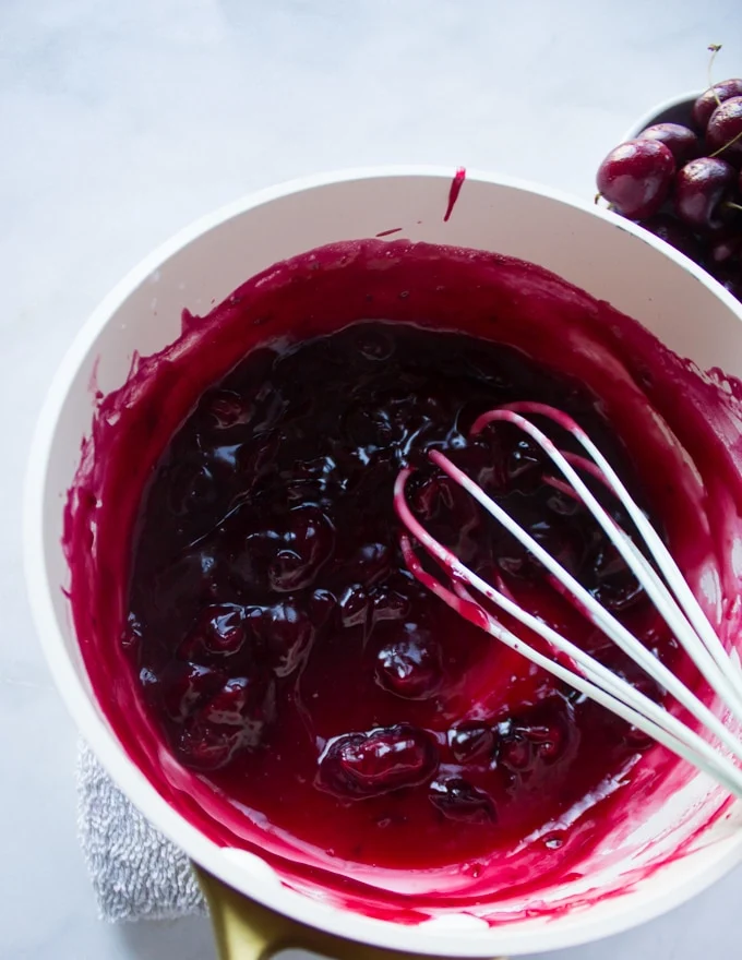 A pot with the cherry pie filling cooked and ready with a whisk in the pan