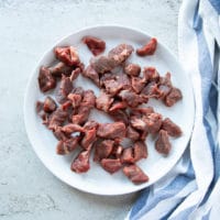 Beef tips on a white plate on a marble with a tea towel showing the cut of meat