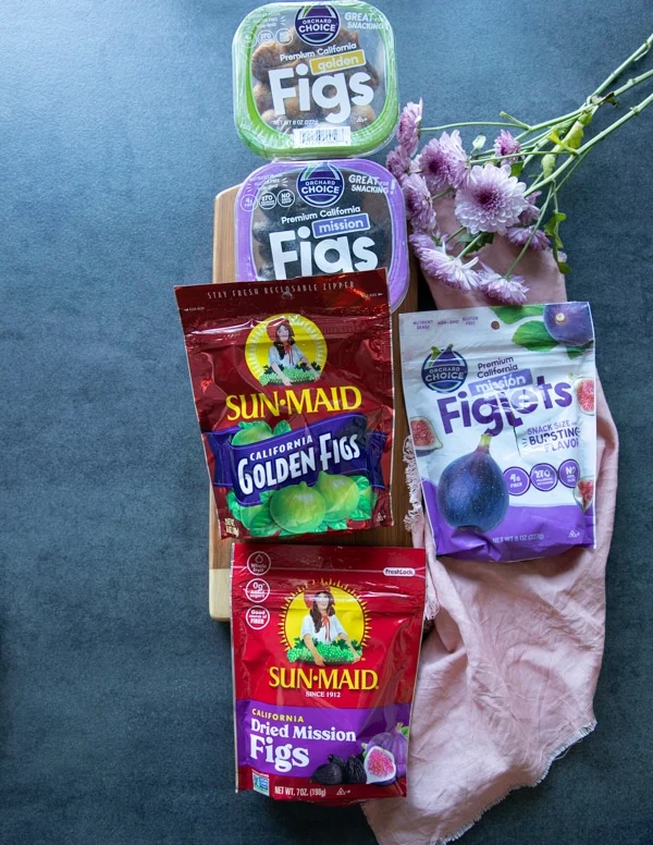 A collection of California dried figs and the different types of them on a wooden board and a pink tea towel around it