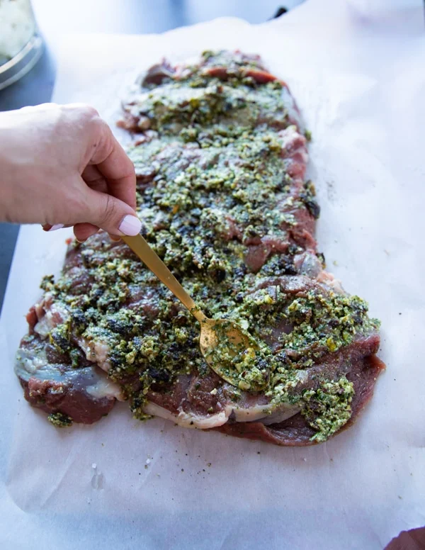 A hand holding a spoon and spreading the filling over the boneless leg of lamb