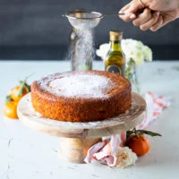 A hand dusting some confectioner's sugar right over the cake for a final finish
