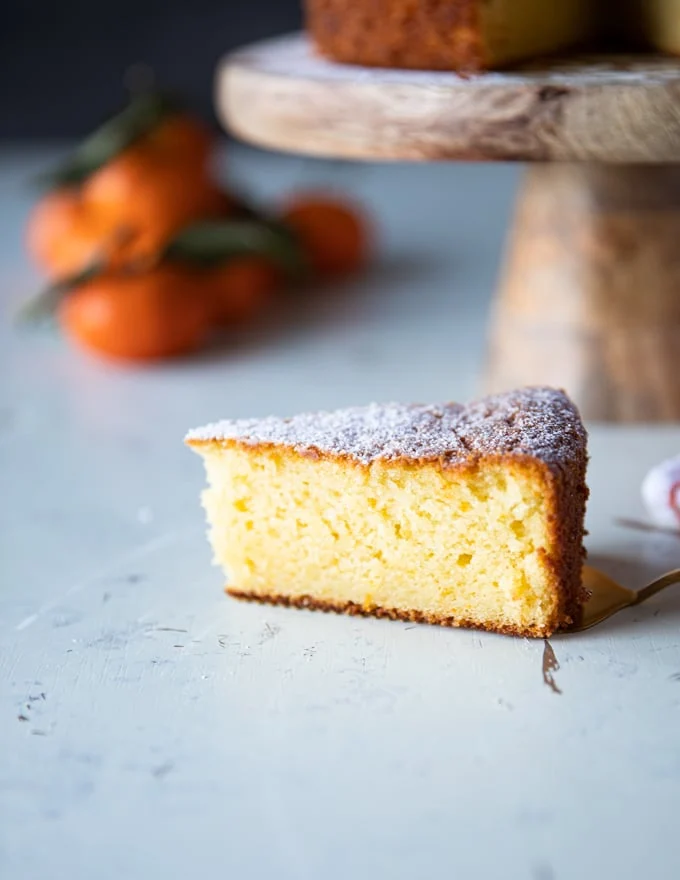 A slice of olive oil cake on a white board close up showing how moist and fluffy it is