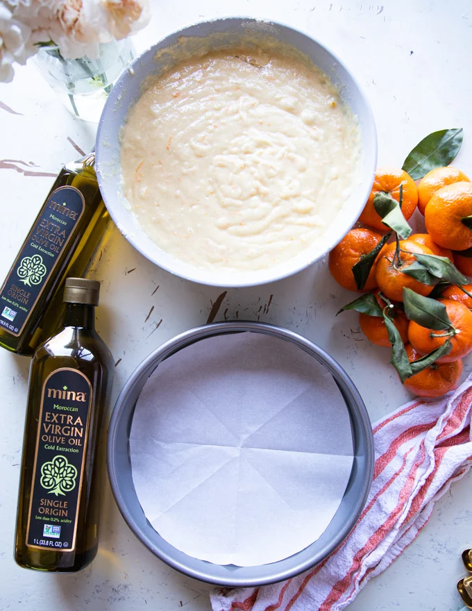 The cake ingredients all mixed in a bowl and a 9 inch cake pan is lined with parchment paper ready for the batter
