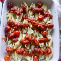 Layered ingredients for stuffed ricotta shells including pasta, tomatoes, sauce and cheese in a white dish.