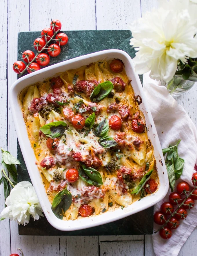 finished ricotta stuffed shells dish in a white baking dish on a table with tomatoes and flowers.