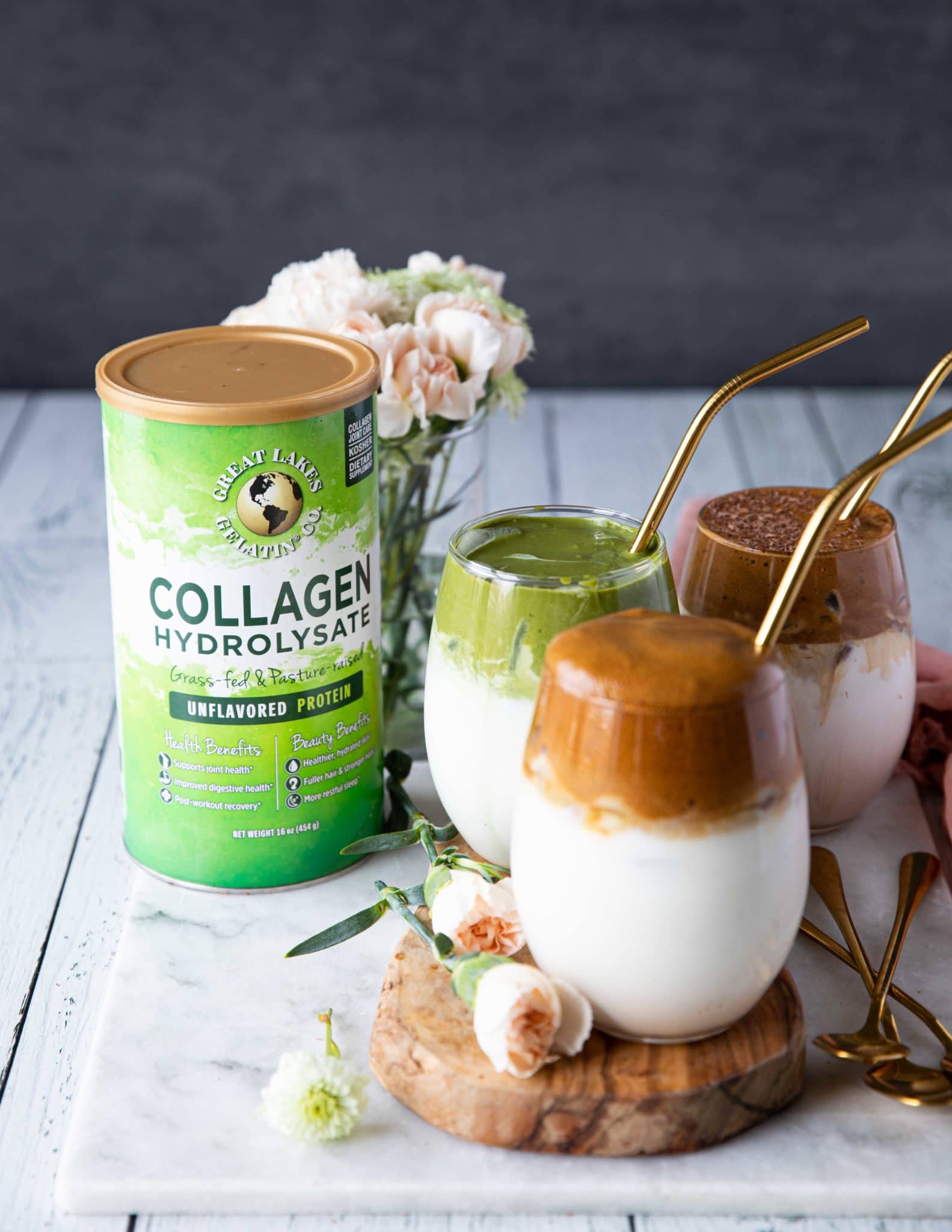 3 cups of dalgona coffee over a wooden board with straws and a flower vase in the back