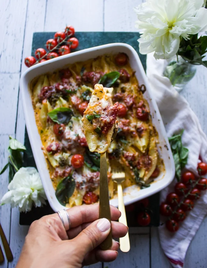 A hand holding a stuffed shell showing the ricotta filling and soft pasta texture