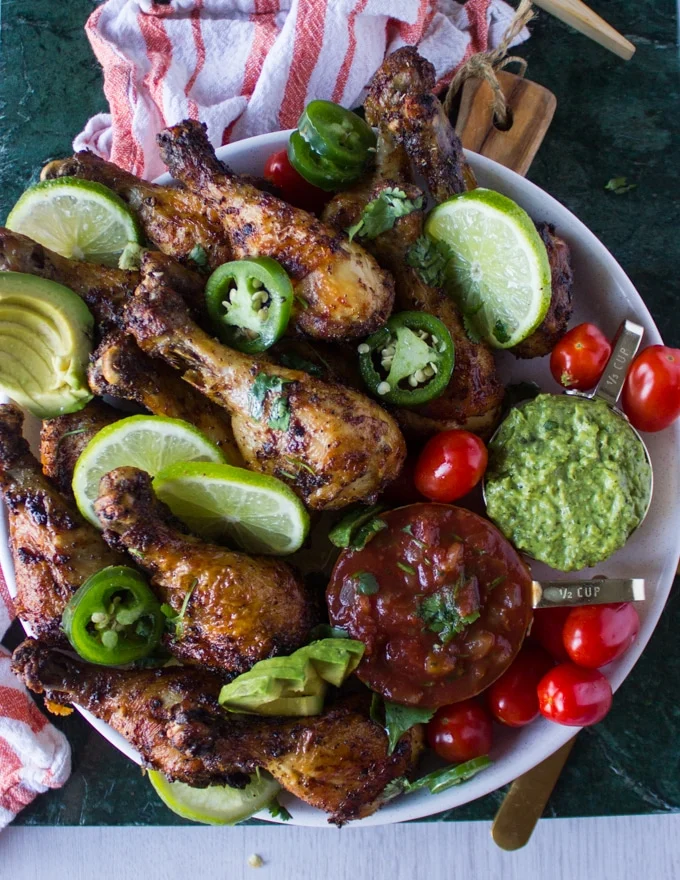 A full plate of air fryer chicken legs served with tomatoes, avocados, lime slices, guacamole and salsa