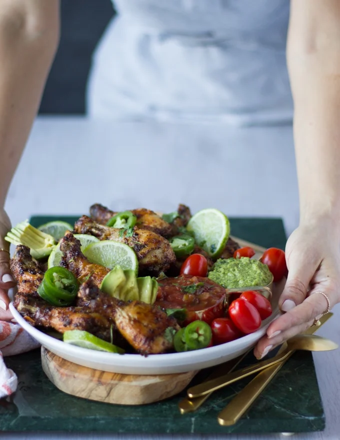hand holding a plate of air fryer chicken recipe with tomatoes, avocados, lime wedges on a wooden board